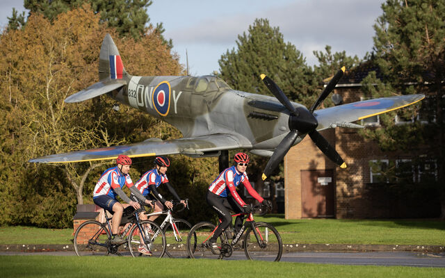3 cyclists on bikes in front of Spitfire at RAF Digby