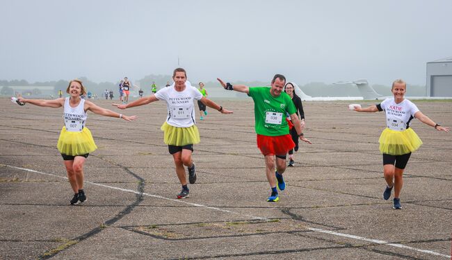 Runners in tutus with arms out like planes